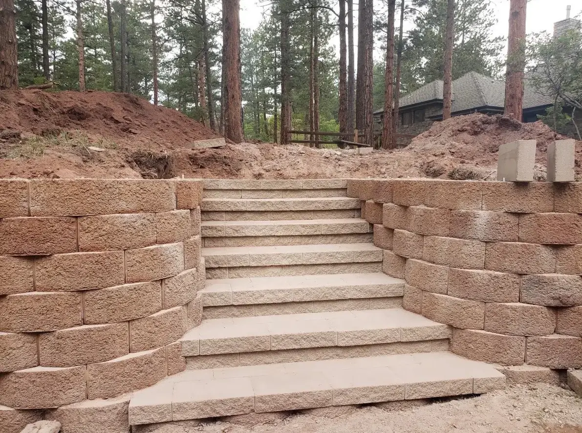 Block retaining wall with stone steps in wooded area